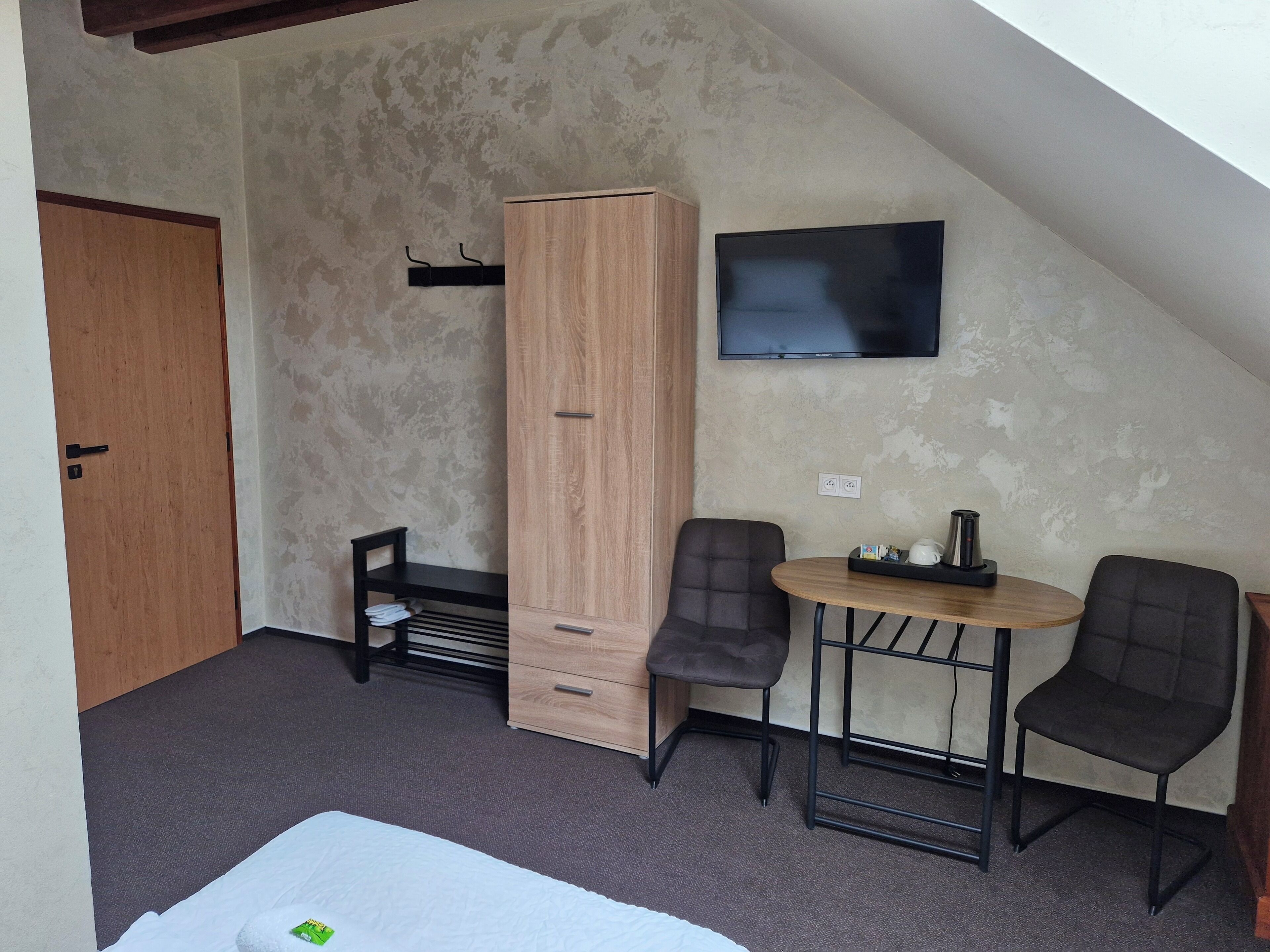 Een kleine, gemeubileerde kamer met een bed, een houten garderobe, een televisie en twee stoelen rondom een klein tafeltje.