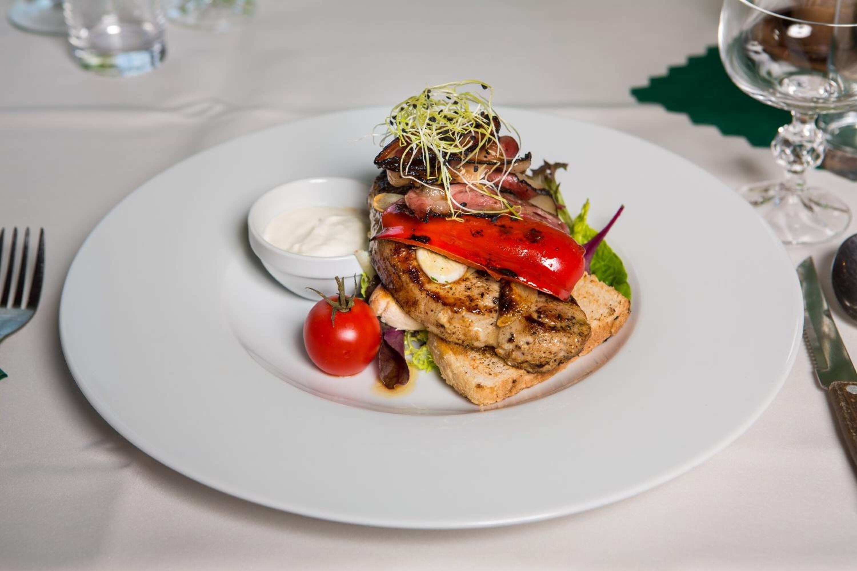 Un plato con pollo a la parrilla, verduras y un recipiente pequeño con salsa.