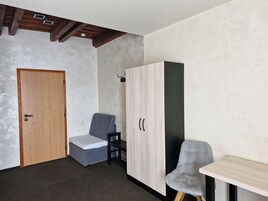 Una habitación con puerta de madera, una silla gris, un armario y una mesita.