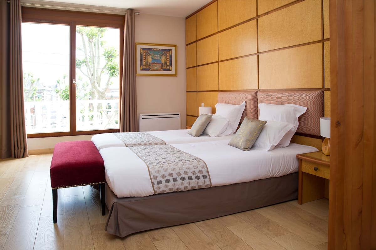 A hotel room with two beds, a large window, and a view of the outside.