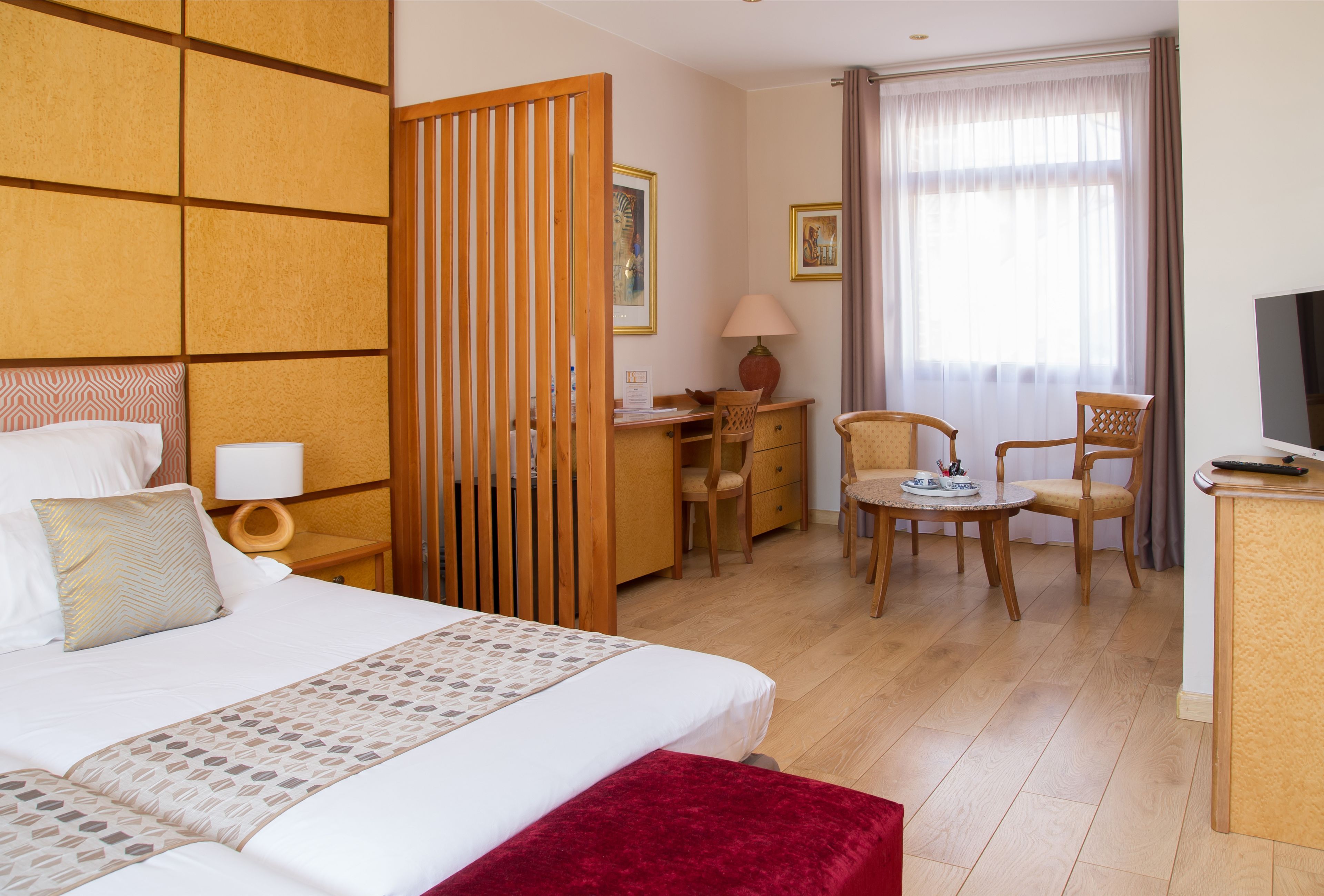 Habitación de hotel con una cama grande, un escritorio, dos sillas, un televisor y una ventana con cortinas.