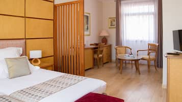Habitación de hotel con una cama grande, un escritorio, dos sillas, un televisor y una ventana con cortinas.