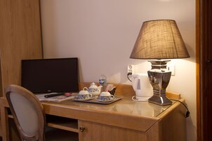 Un escritorio de madera con una computadora portátil, una lámpara, un hervidor de agua, tazas y una tetera.