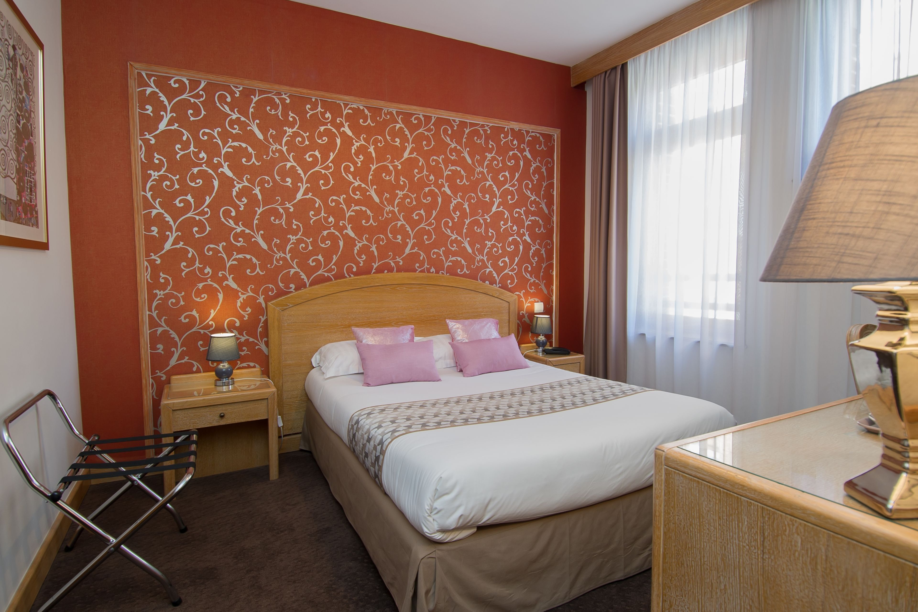 Een hotelkamer met een groot bed, een houten hoofdeinde, een nachtkastje met een lamp, een stoel en een decoratief paneel aan de muur.