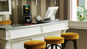 Un espace bar avec des tabourets, une machine à café et des étagères remplies de bouteilles et de verres.