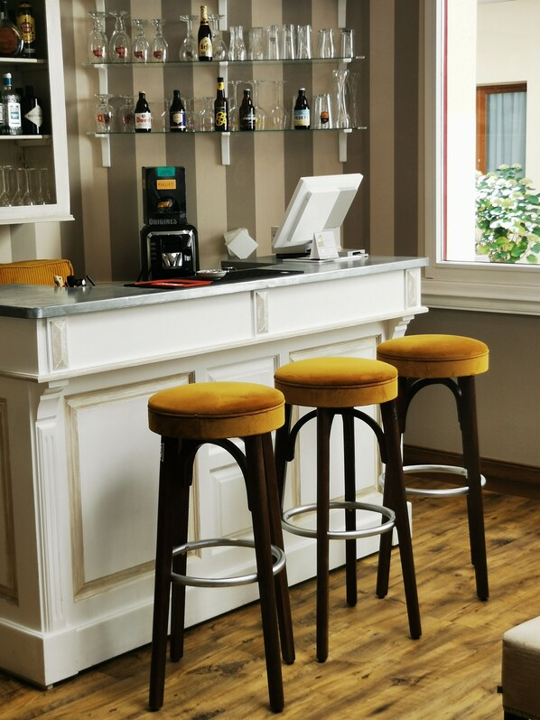 Una zona de bar con taburetes, una cafetera y estantes con botellas y vasos.
