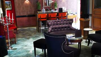 A lobby with a marble floor, a tufted armchair, a bar area with orange chairs, and a red wall with a mirror.