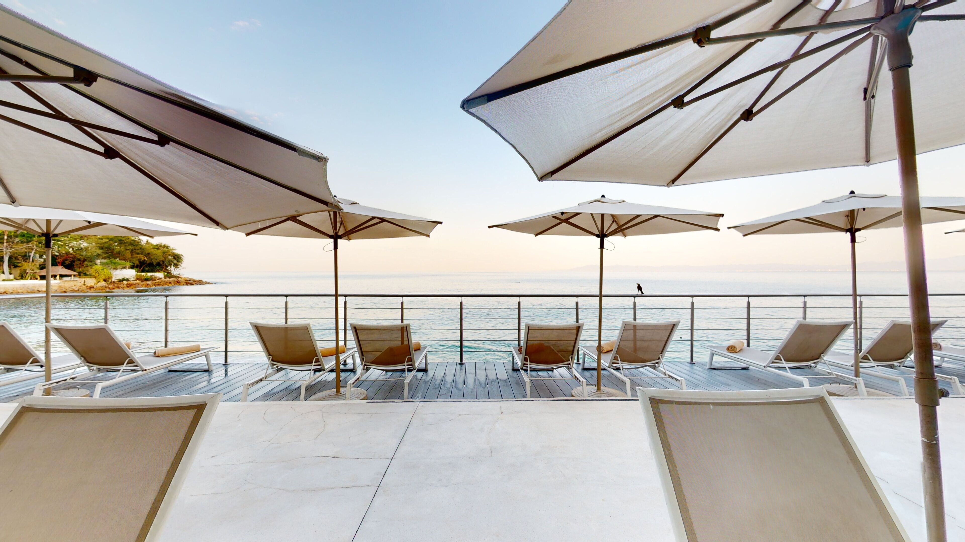 A deck with sun loungers and umbrellas overlooking a body of water.