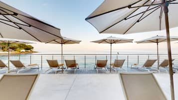 A deck with sun loungers and umbrellas overlooking a body of water.
