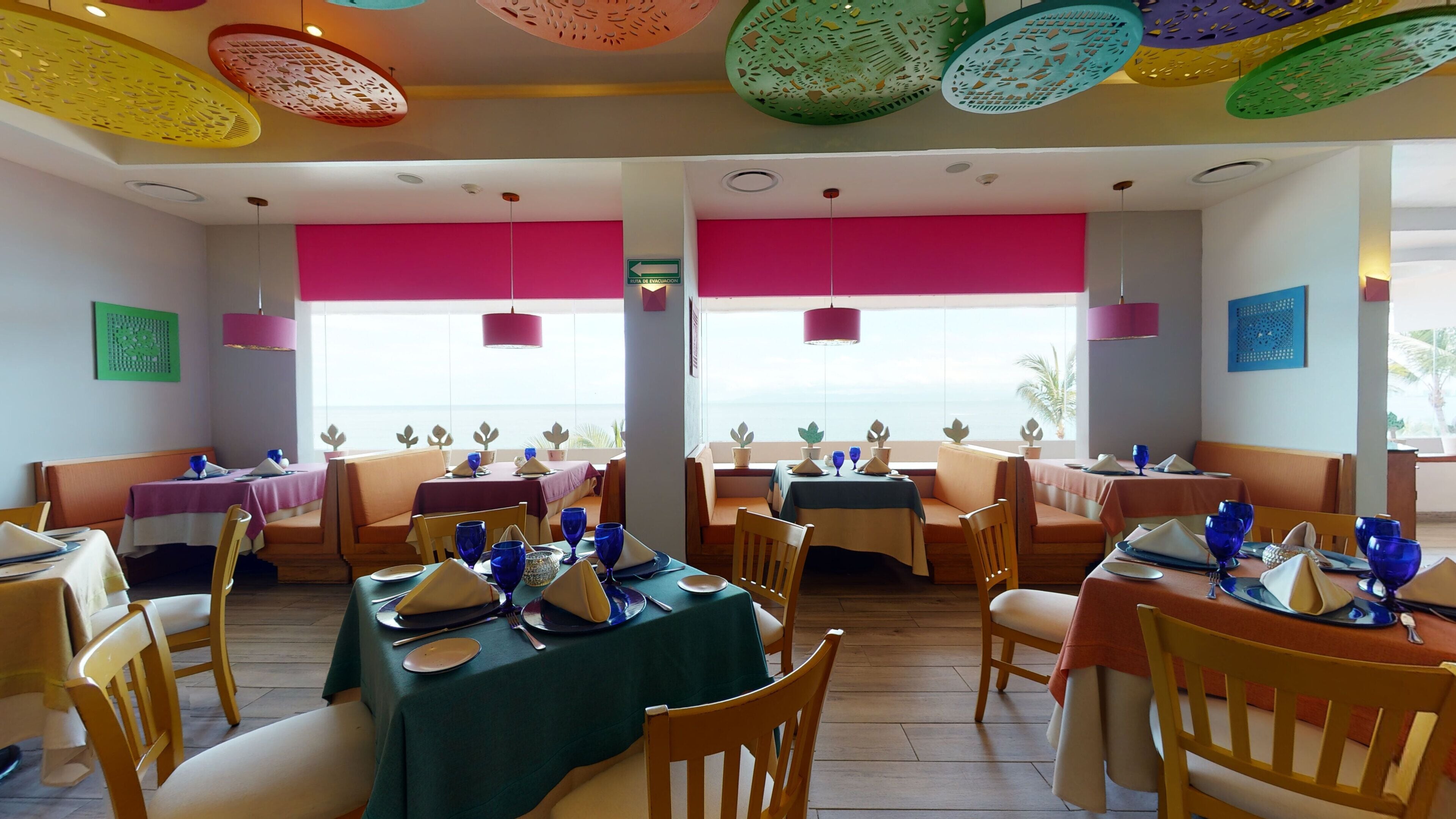 A restaurant with tables set for dining, chairs, and a view of the sea.