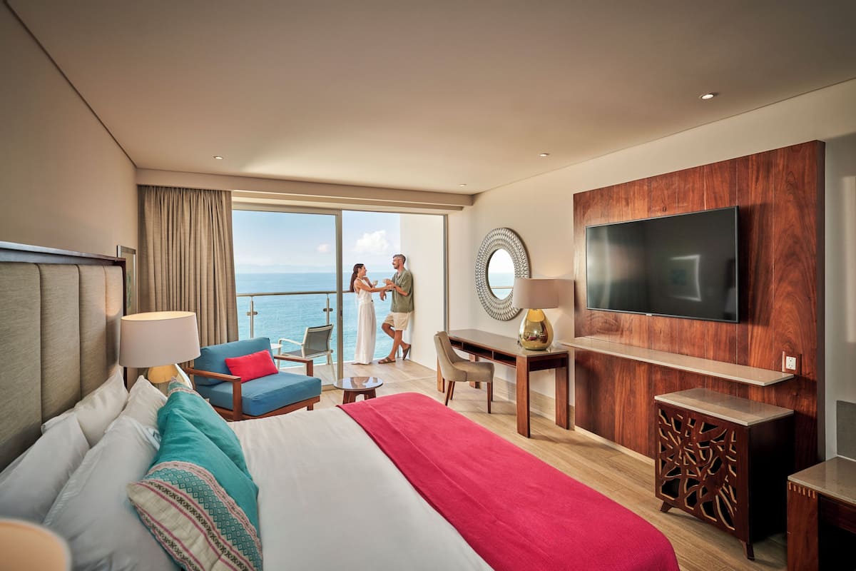 Une chambre d’hôtel moderne dotée d’un grand lit, d’une télévision, d’un bureau et d’un balcon offrant une vue sur la mer.