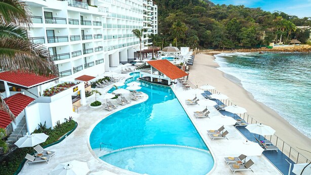 A resort with a large swimming pool, beachside lounge chairs, and a hotel building with multiple balconies.