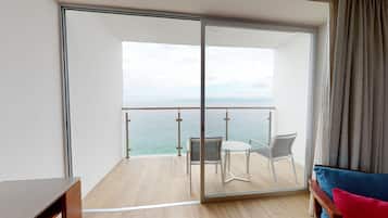 A balcony with a glass door, a table, two chairs, and a view of the sea.