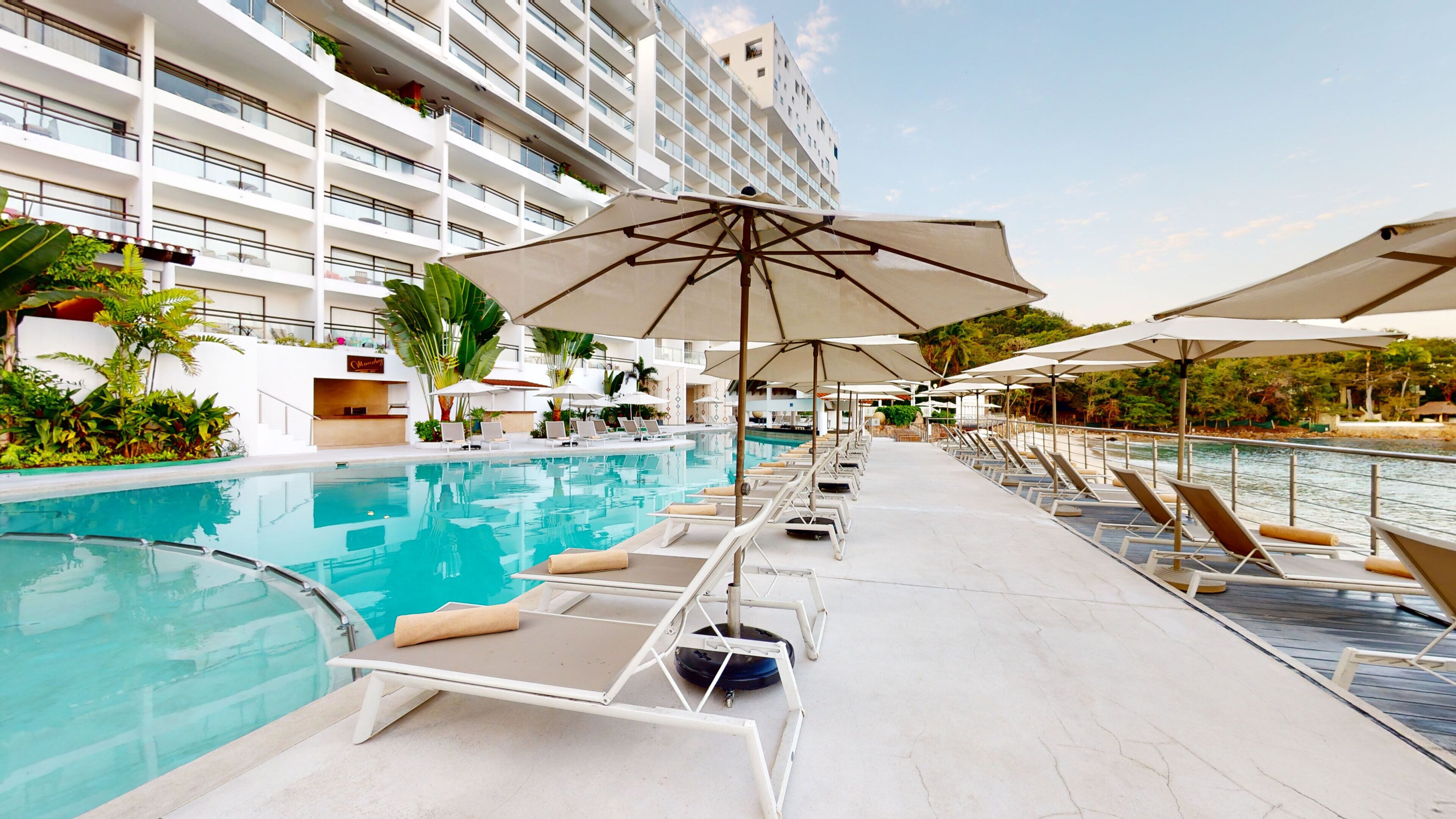 A poolside area with lounge chairs and umbrellas, a pool, and a high-rise building in the background.