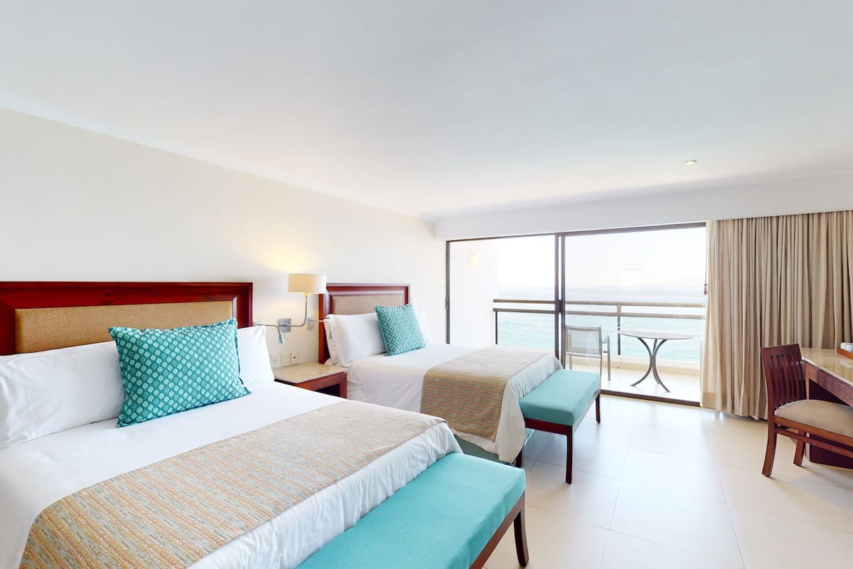 Une chambre d’hôtel avec deux lits, un bureau, une chaise et un balcon donnant sur la mer.