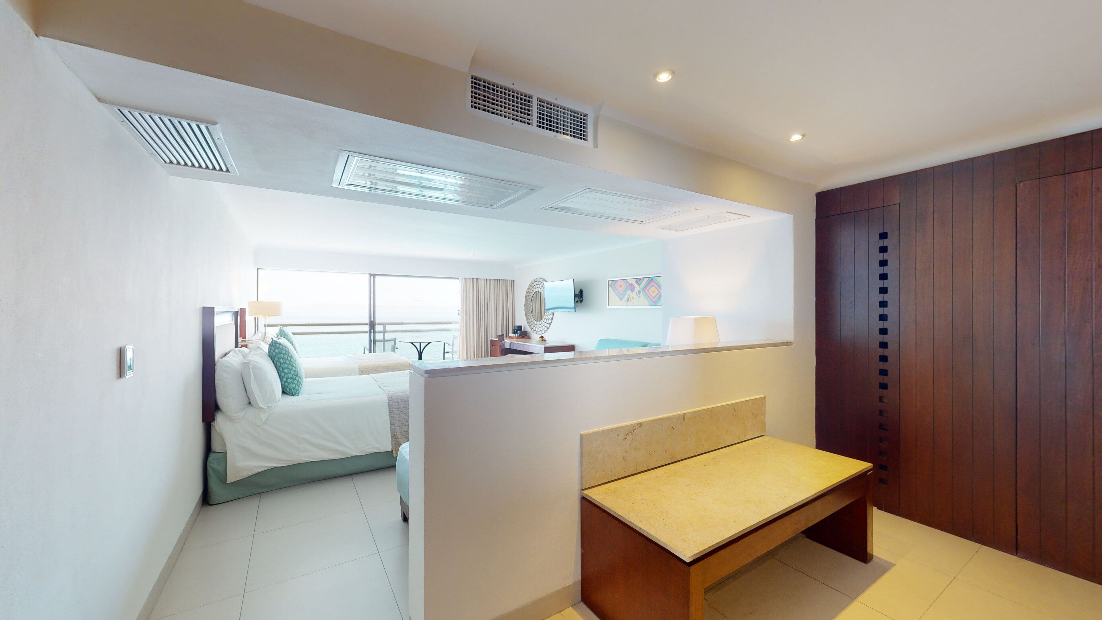 Habitación de hotel con cama, escritorio, banco, televisor y ventana grande.