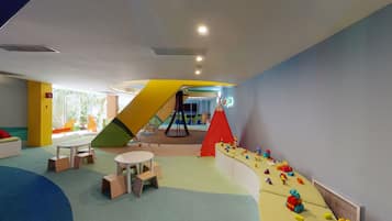 A children's play area with a slide, climbing wall, and soft play surfaces.