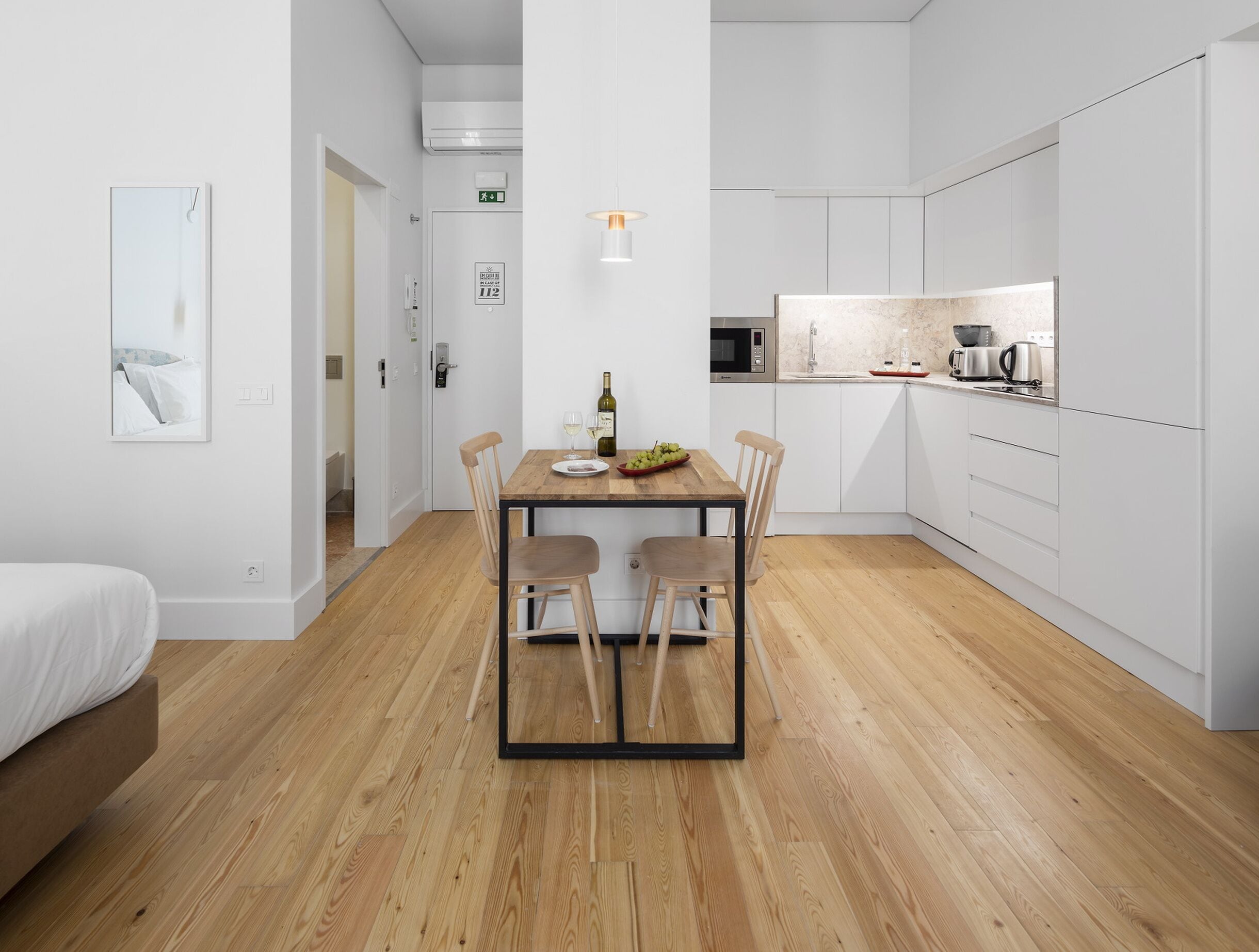 A modern kitchen with white cabinets, a wooden dining table, and a microwave.
