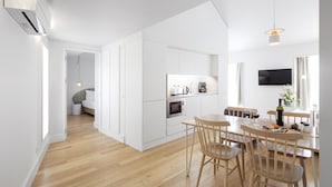 A modern kitchen with white cabinetry, a dining area with wooden chairs, and a flat-screen TV mounted on the wall. -  LSA Benformoso by Numa (Lisbon)