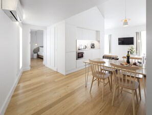 A modern kitchen with white cabinetry, a dining area with wooden chairs, and a flat-screen TV mounted on the wall. -  LSA Benformoso by Numa (Lisbon)