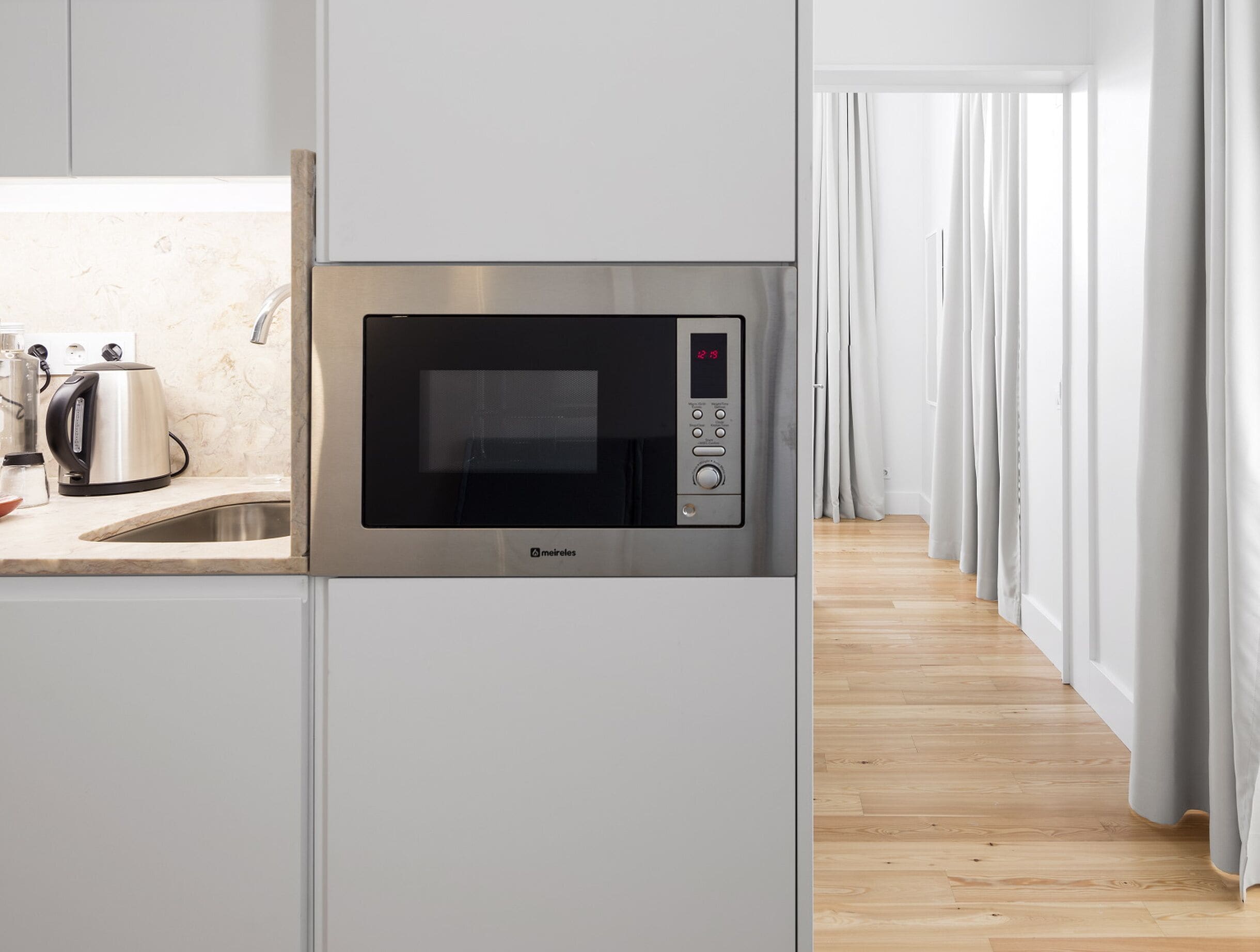 Une cuisine moderne équipée d’un four à micro-ondes encastré, d’une bouilloire et d’un évier.