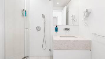 A modern bathroom with a glass shower enclosure, a sink with a marble countertop, and a mirror.