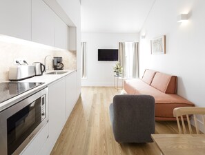 A modern kitchen with a toaster, kettle, and coffee maker, a sofa, and a flat-screen TV mounted on the wall. -  LSA Benformoso by Numa (Lisbon)