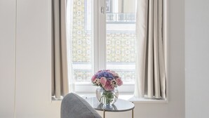 A room with a window, a chair, a small table with a vase of flowers, and a lamp. -  LSA Benformoso by Numa (Lisbon)