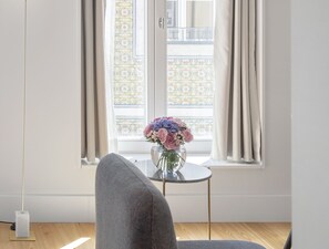 A room with a window, a chair, a small table with a vase of flowers, and a lamp. -  LSA Benformoso by Numa (Lisbon)