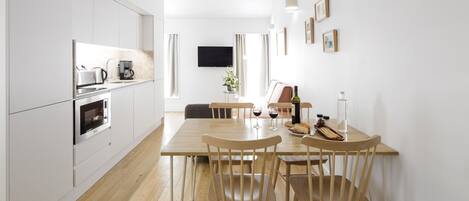 Una cocina moderna con armarios blancos, horno integrado y un comedor con mesa y sillas de madera.