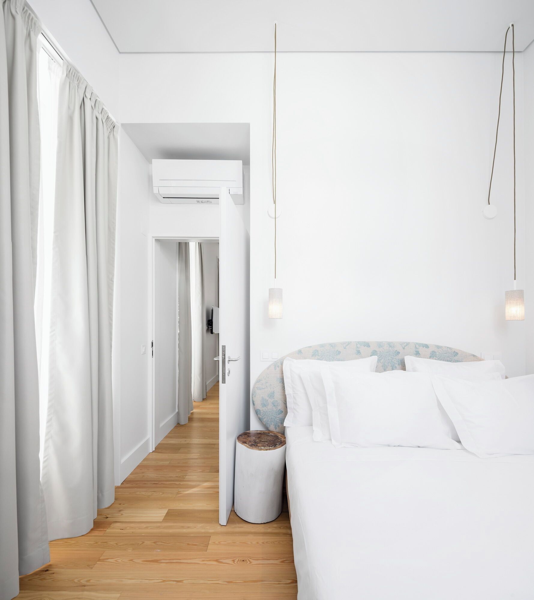 Un dormitorio minimalista con cama, cortinas, equipo de aire acondicionado y un pasillo.