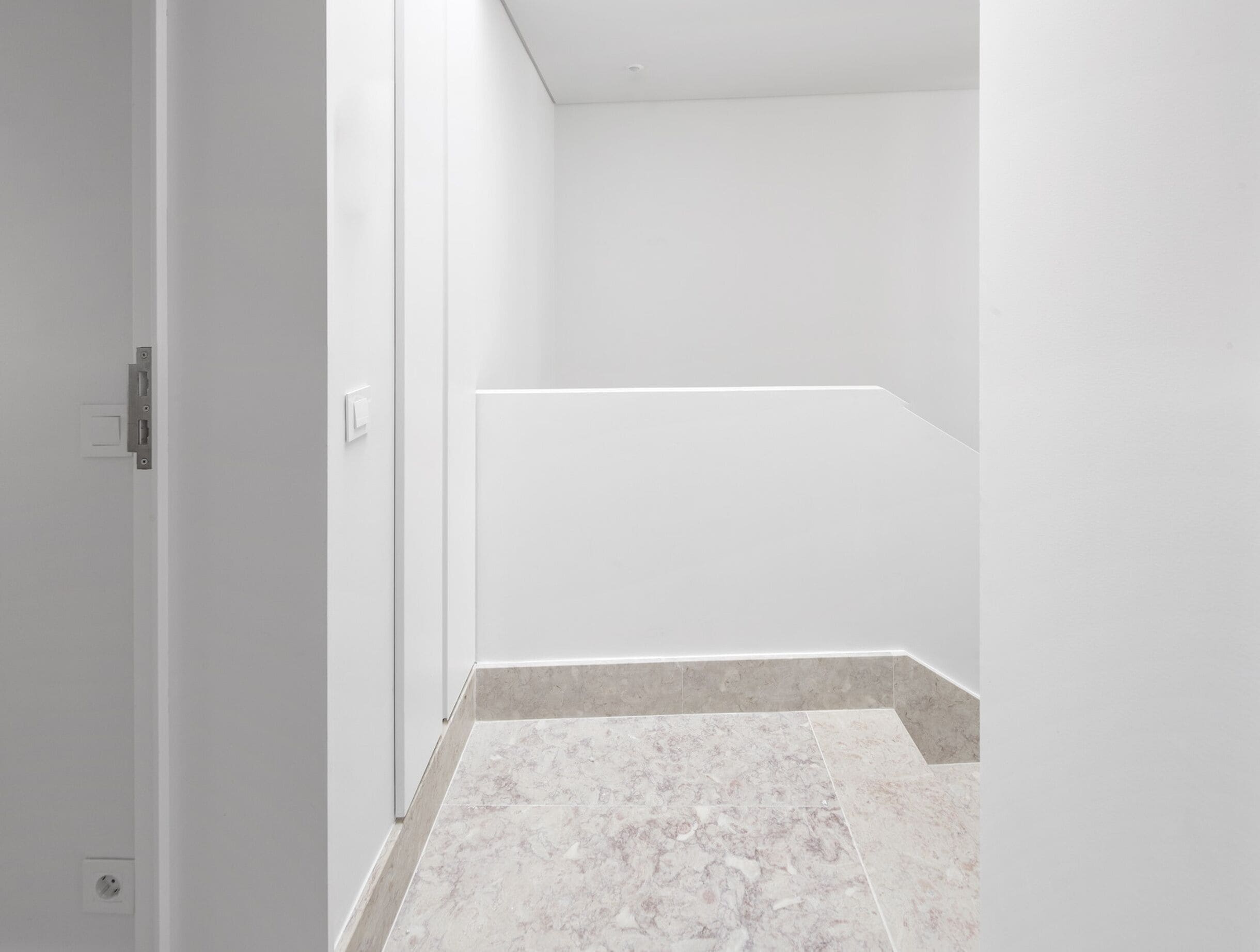 A hallway with a door, a light switch, and a tiled floor.