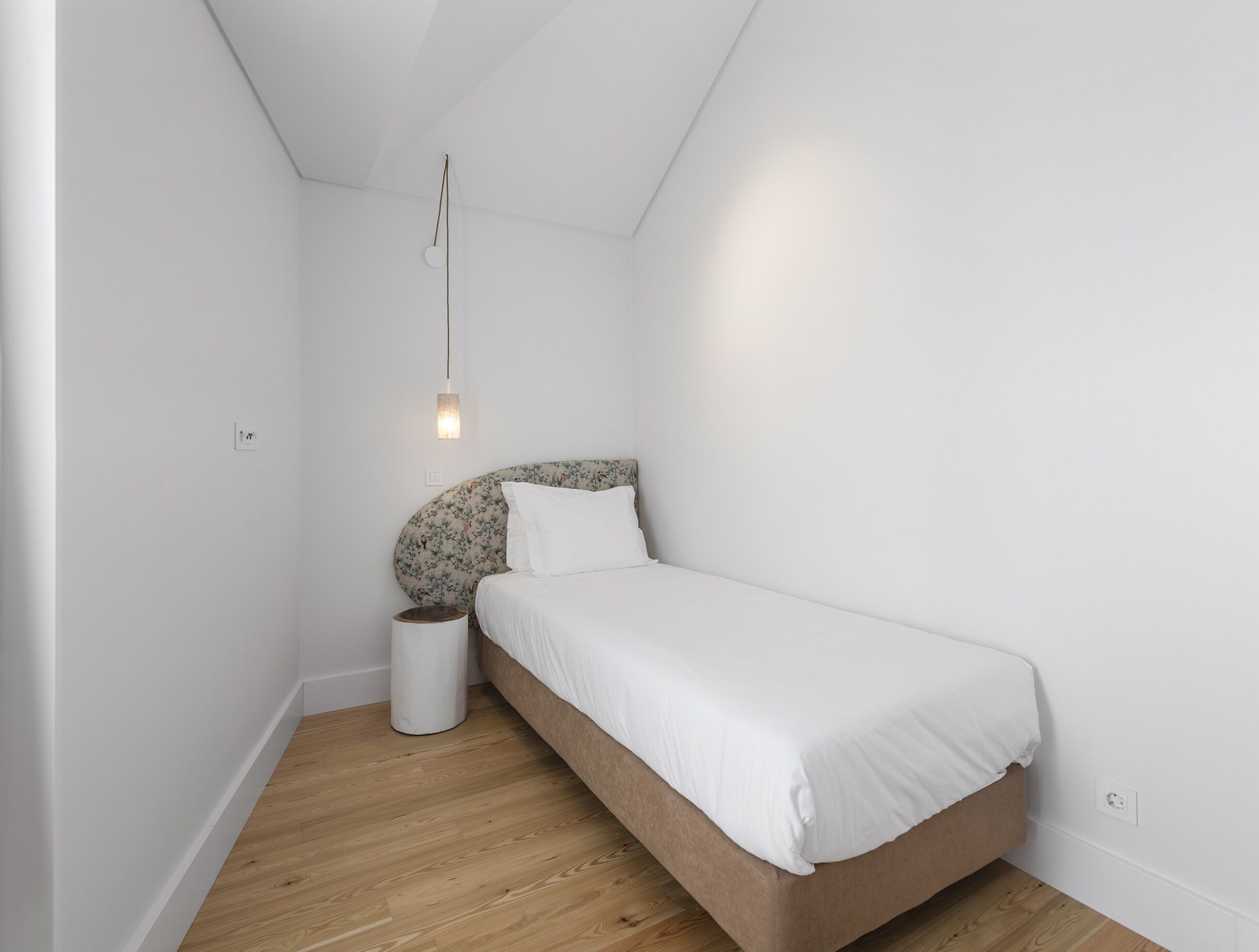 Une petite chambre à coucher, bien rangée, avec un lit simple, une lampe de chevet et une poubelle.