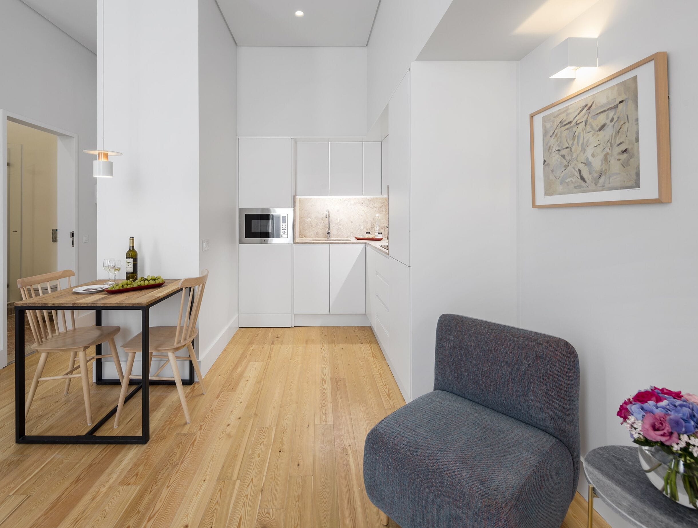 Un espace de vie compact comprenant un coin repas, une kitchenette et un fauteuil gris.
