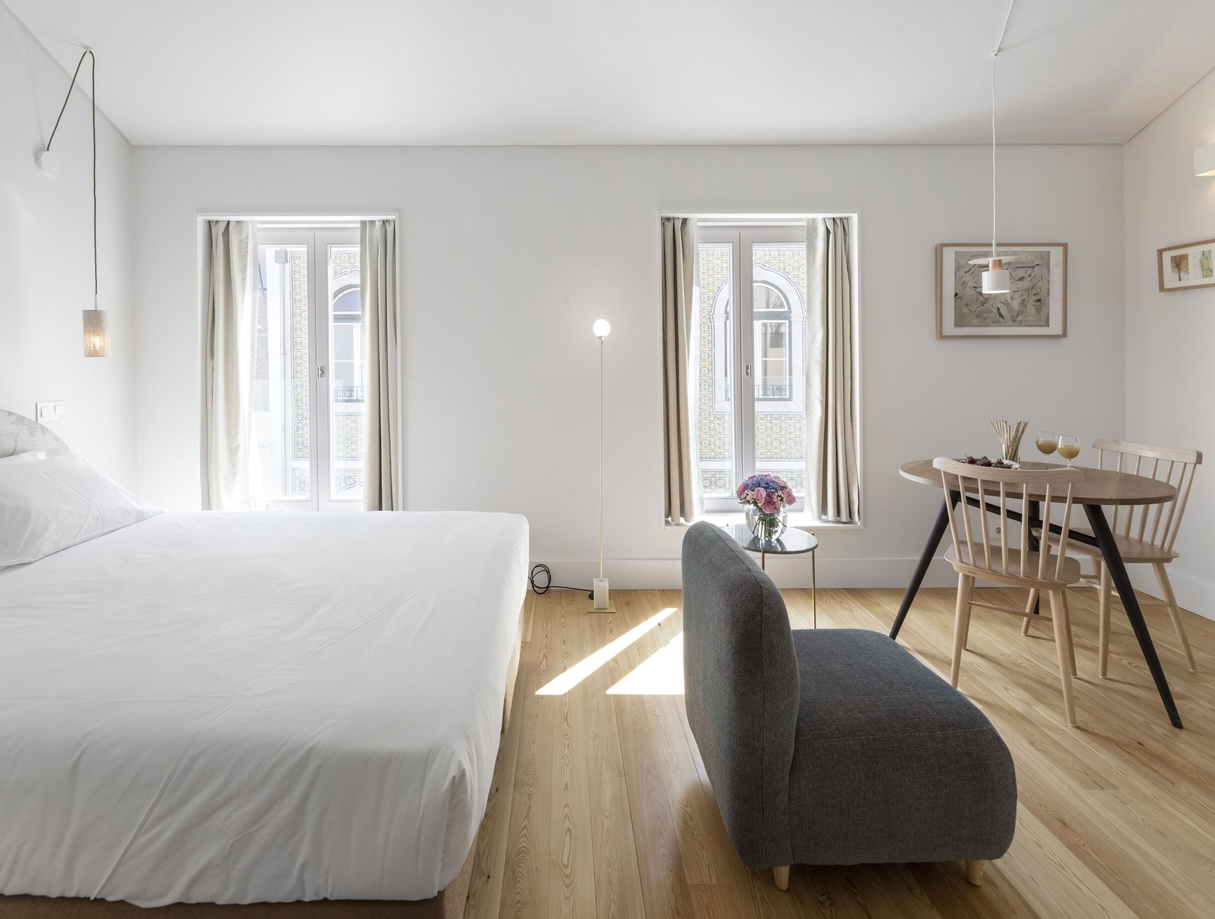 Una habitación de hotel con una cama, una mesa de comedor con sillas, un florero con flores y un cuadro en la pared.
