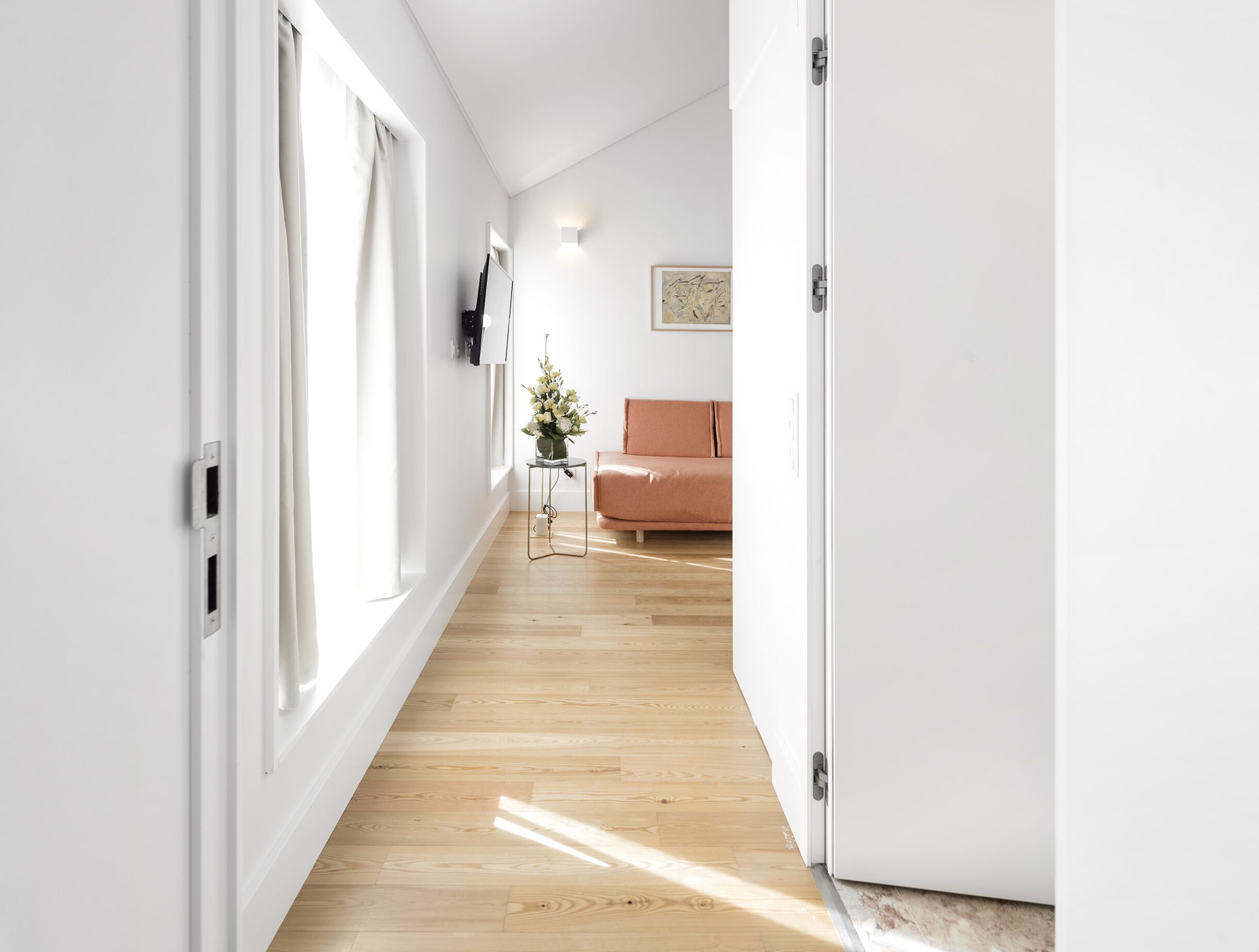 A hallway with wooden flooring, a white door, and a beige sofa in the background.
