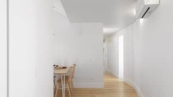 A narrow hallway with a dining area featuring a wooden table and chairs, white walls, and a wooden floor.