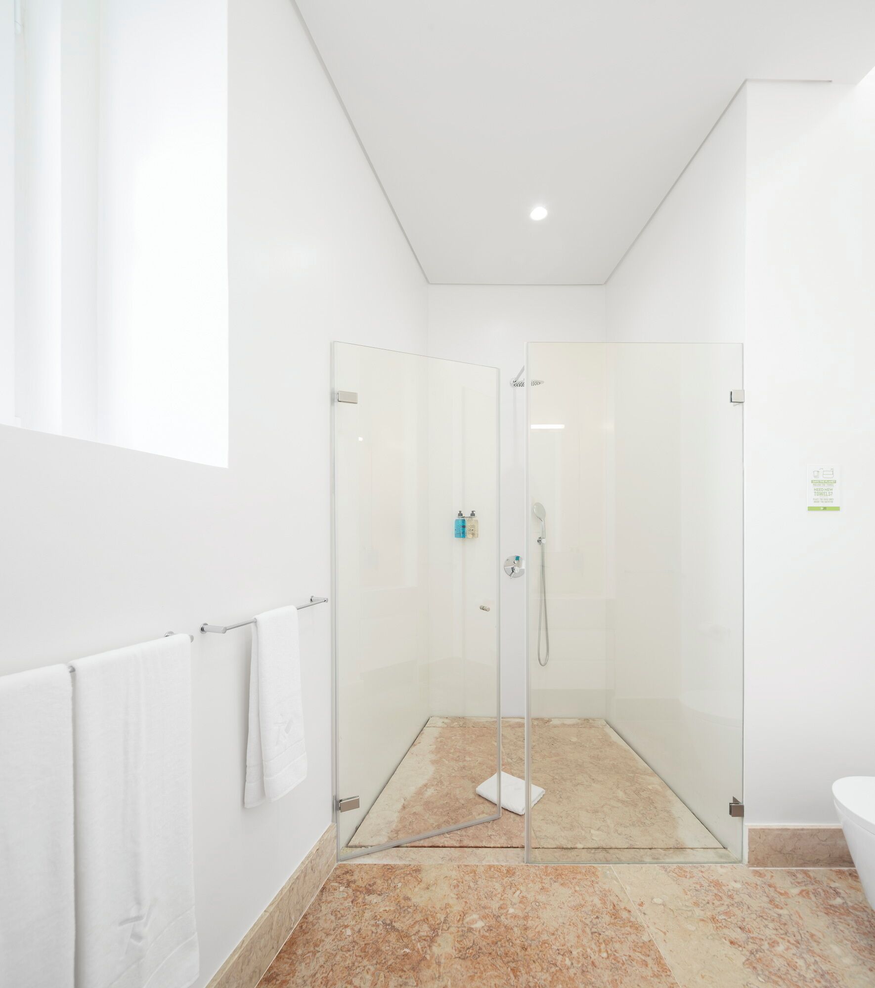 Een moderne badkamer met een douchecabine van glas, marmeren vloeren en een wit toilet.