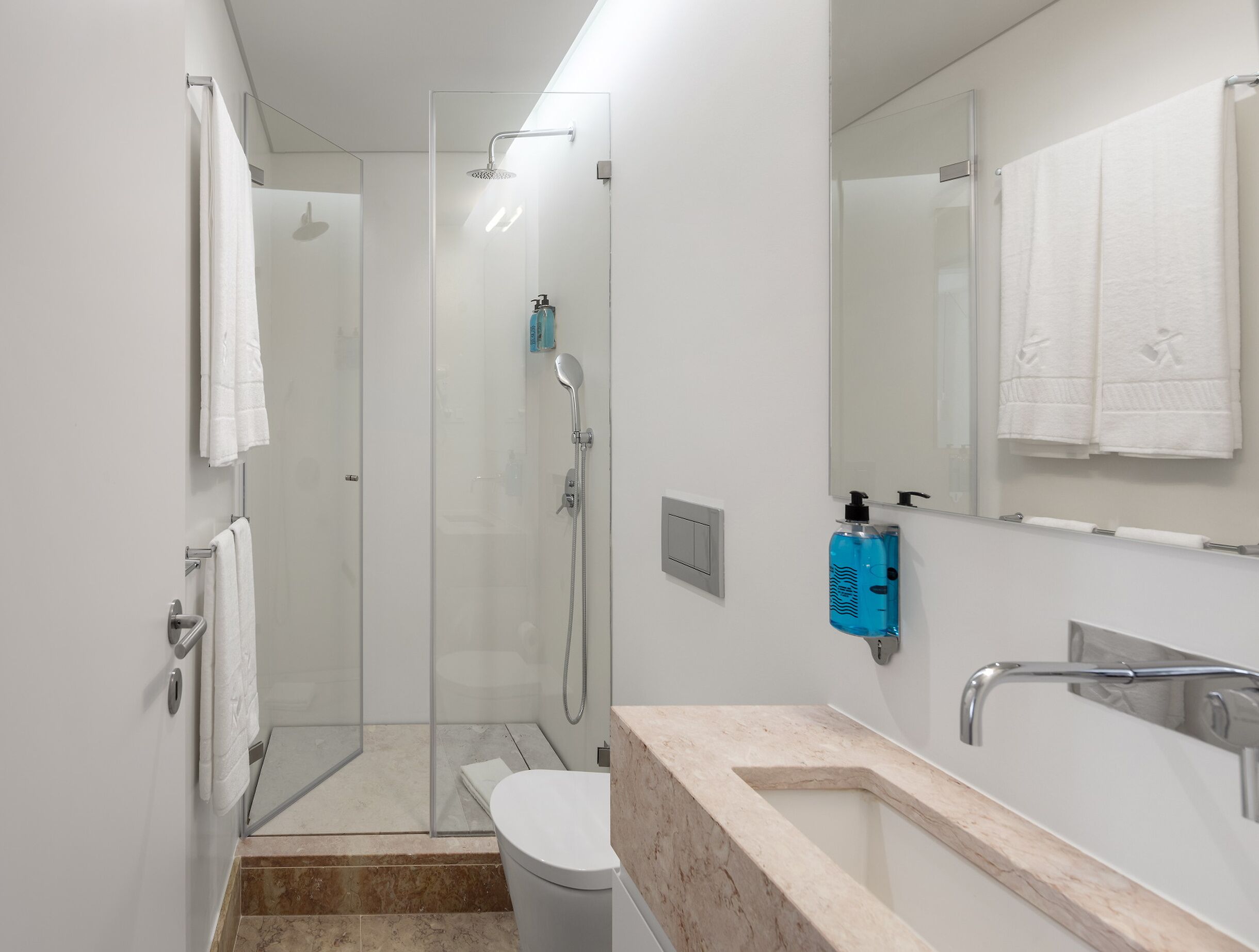 Un baño moderno con cabina de ducha de vidrio, inodoro, lavamanos con encimera de mármol y espejo.