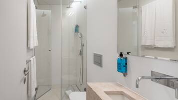 Un baño moderno con cabina de ducha de vidrio, inodoro, lavamanos con encimera de mármol y espejo.