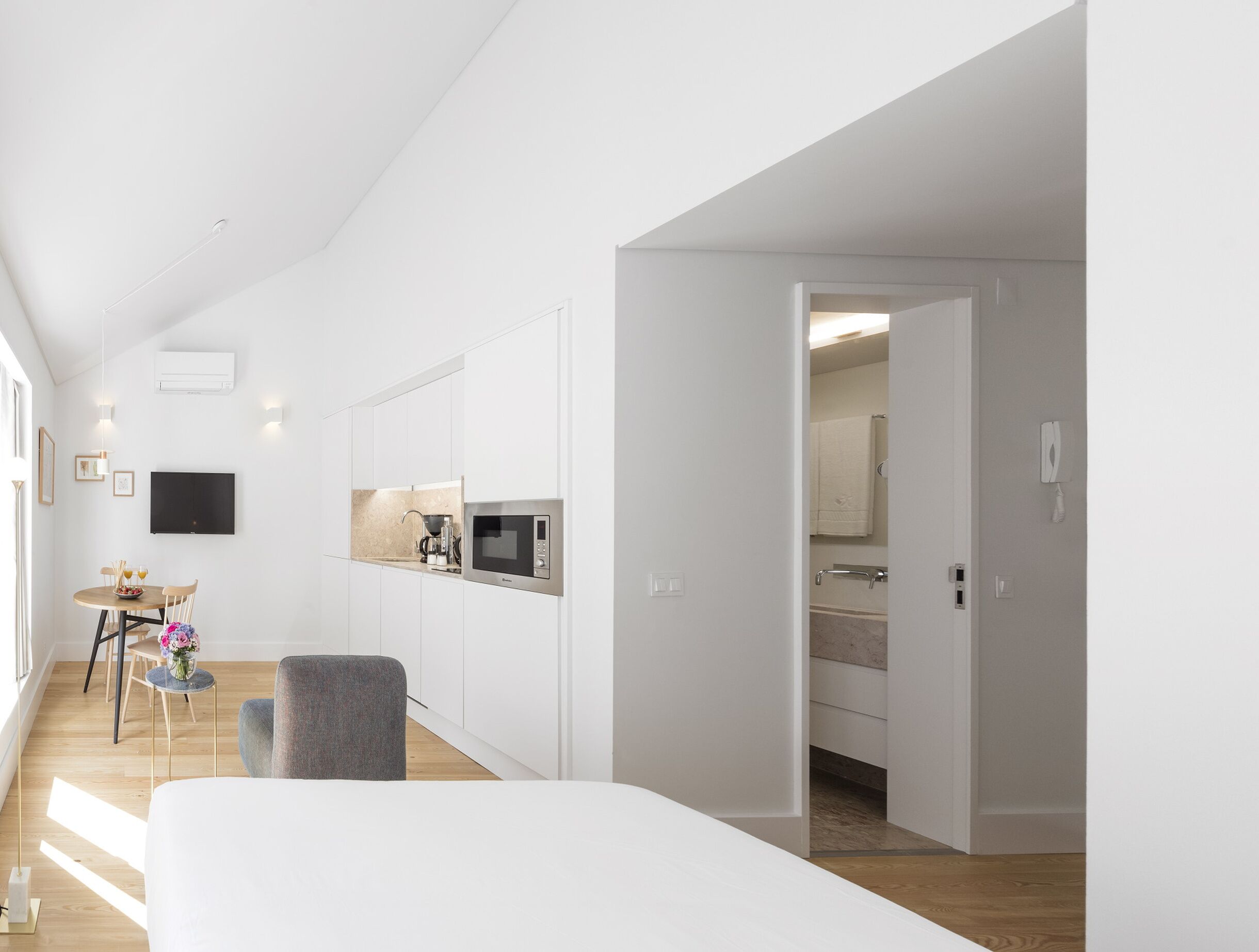 Een moderne, minimalistisch ingerichte slaapkamer met een groot bed, een klein nachtkastje en een stoel.