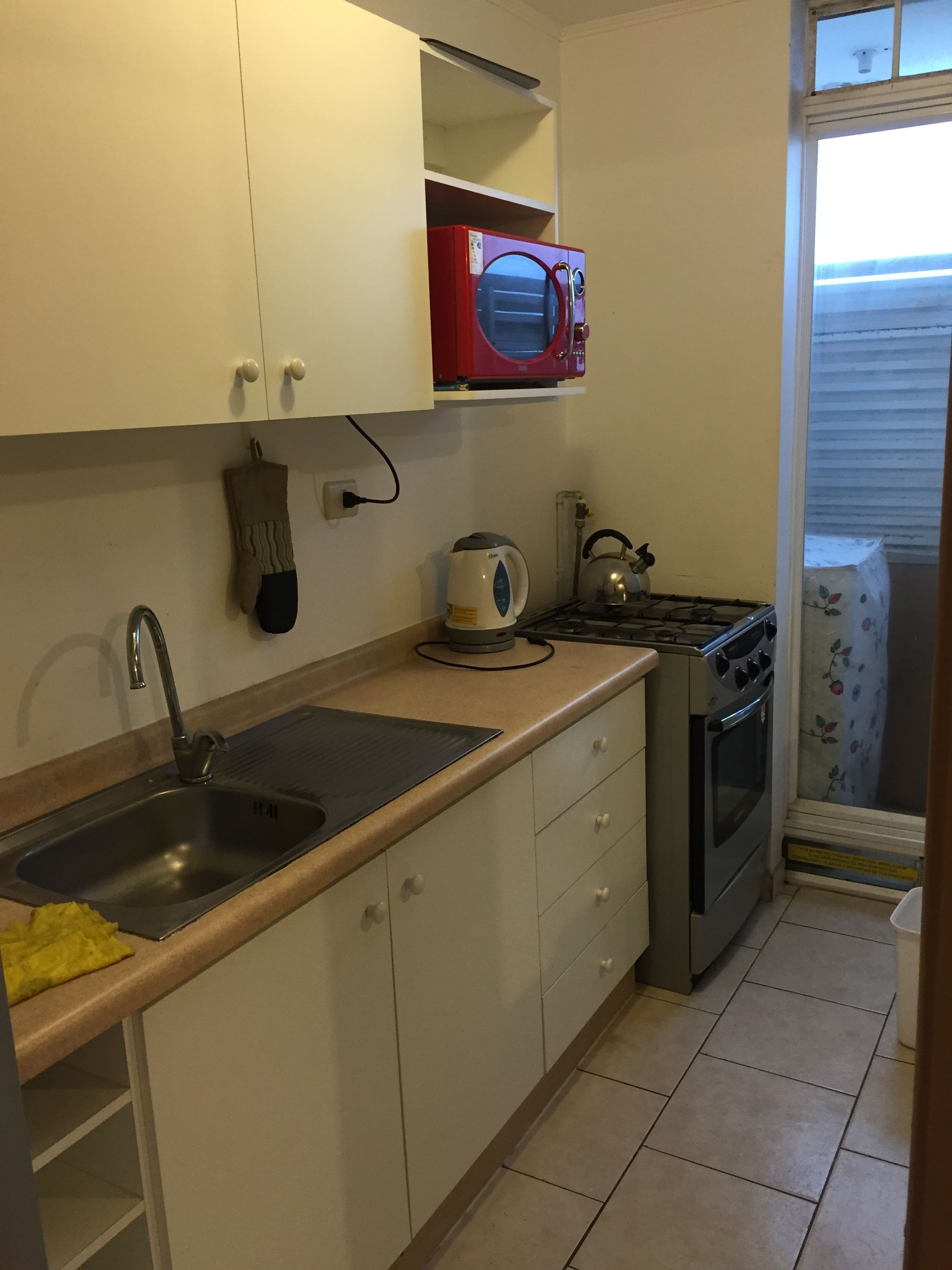 A compact kitchen with a sink, stove, kettle, and microwave.