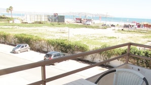 A balcony with a white table and wicker chairs, overlooking a beach with parked cars and a distant view of the ocean. - 61.- HNA Reinos Italia (La Serena)