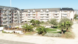 A multi-story hotel with balconies, a parking area, and landscaped gardens with palm trees. - 61.- HNA Reinos Italia (La Serena)