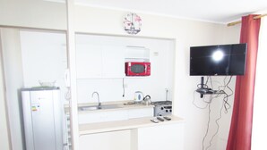 A compact kitchenette with a refrigerator, microwave, sink, and stove. A flat-screen TV is mounted on the wall. - 61.- HNA Reinos Italia (La Serena)