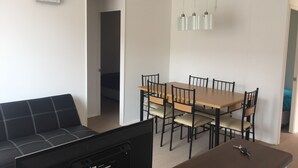 A compact living space with a sofa, a dining table with chairs, a small TV, and a ceiling light fixture. - 51.- HNA Reinos Celta (La Serena)