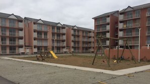 A playground with a slide and swings in front of a multi-story residential building. - 51.- HNA Reinos Celta (La Serena)