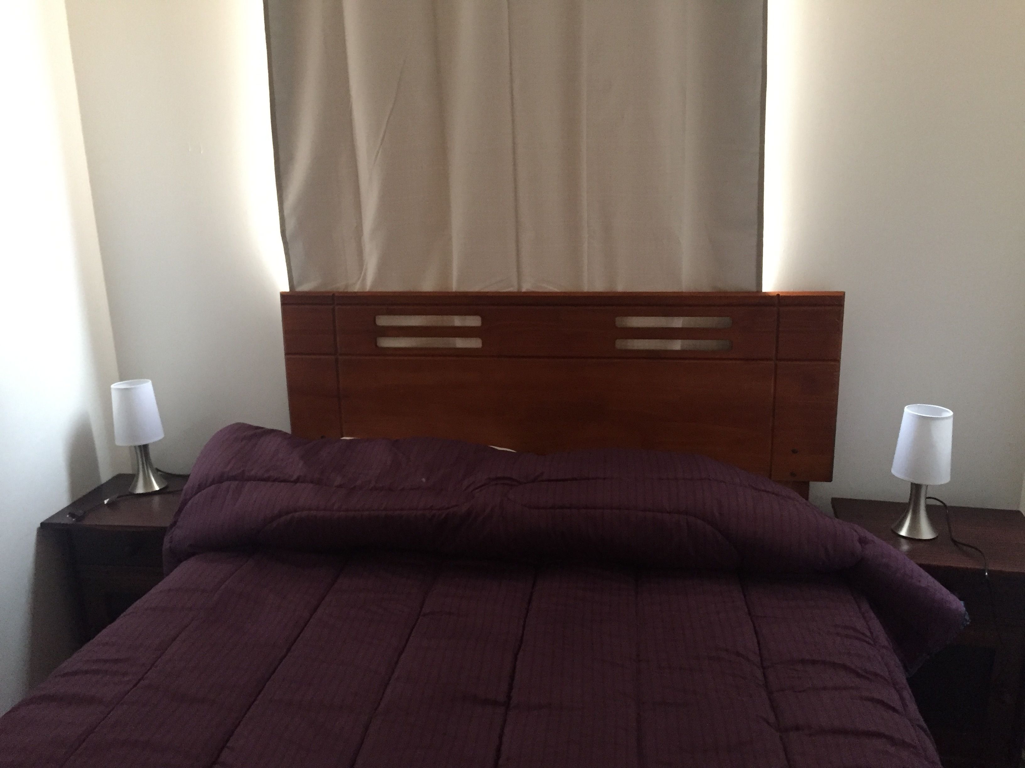 Uma cama com cabeceira, duas mesas de cabeceira e duas luminárias.