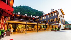 A hotel with a covered outdoor dining area, multiple floors, and a mountainous backdrop. - Flora Uzungol Resort Hotel (Çaykara)