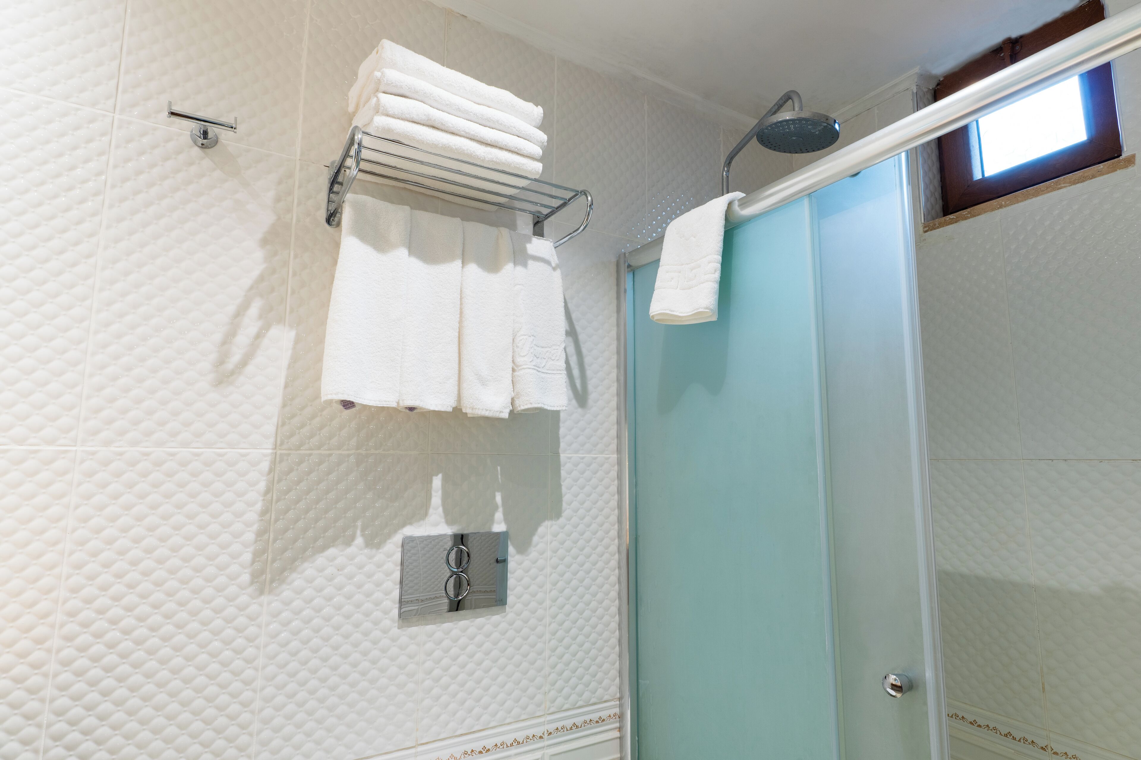 A bathroom with a glass shower door, a towel rack with folded towels, and a wall-mounted towel dispenser.